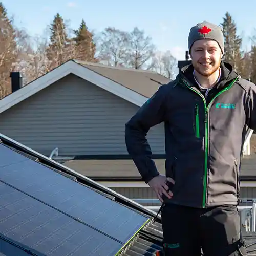 Solceller på ett tak utomhus och en man från SmartTech Energy som håller i ett räcke och tittar in i kameran